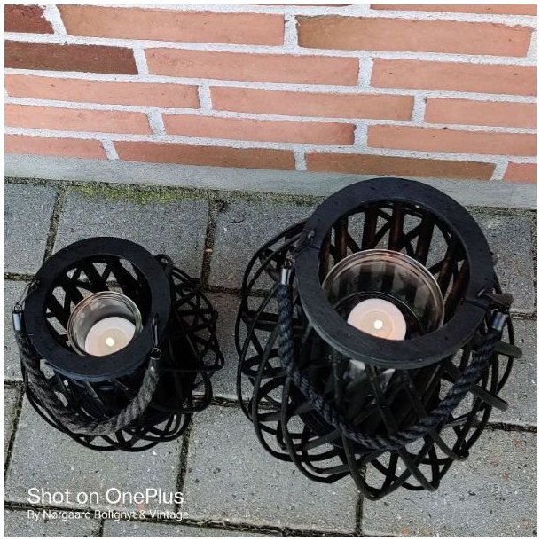 En oppefra-og-ned-visning af to sorte fletlanterner p� en terrakotta-flise, med synlige glasindsatser.