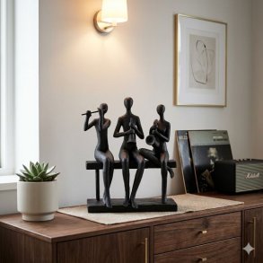 Et stilfuldt indend�rs milj�billede af en m�rk, stiliseret figur i polyresin, der forestiller tre musikere, der sidder p� en b�nk og spiller fl�jte, obo og saxofon. Skulpturen er placeret centralt p� en m�rk tr�sk�nk, flankeret af en sukkulentplante, vinylplader og en retro-h�jttaler, under det varme sk�r fra en v�glampe.