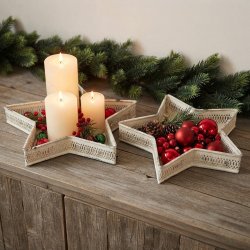 Stemningsfuldt milj�billede af to cremehvide stjernefade i jern p� en tr�sk�nk, dekoreret med bloklys, r�de julekugler og grangren i baggrunden.
