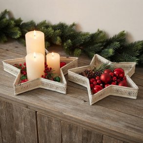 Stemningsfuldt milj�billede af to cremehvide stjernefade i jern p� en tr�sk�nk, dekoreret med bloklys, r�de julekugler og grangren i baggrunden.