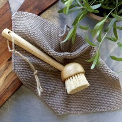 Et milj�billede af en beige strikket karklud placeret p� et k�kkenbord sammen med en opvaskeb�rste i tr� og et sk�rebr�t.