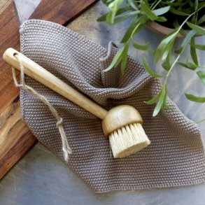 Et milj�billede af en beige strikket karklud placeret p� et k�kkenbord sammen med en opvaskeb�rste i tr� og et sk�rebr�t.