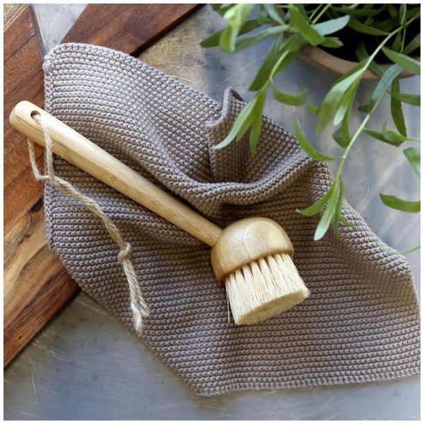Et milj�billede af en beige strikket karklud placeret p� et k�kkenbord sammen med en opvaskeb�rste i tr� og et sk�rebr�t.