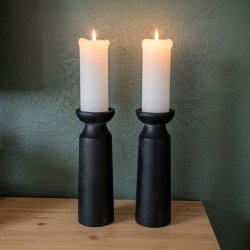 To store, moderne sorte tr�lysestager med t�ndte hvide bloklys st�r side om side p� et lyst tr�kombords. Baggrunden er en m�rk, struktureret salviegr�n v�g, og de to stearinlys kaster et varmt, hyggeligt sk�r.