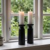 To store, sorte tr�lysestager med t�ndte stearinlys st�r p� en hvid vindueskarm foran et vindue med udsigt til en gr�n have. En lille sukkulent plante i en krukke st�r til venstre.
