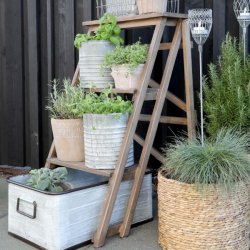 H�j vinkelbillede af den naturfarvede tr�stige p� en terrasse, dekoreret med urtepotter af planter, blomster, krydderurter og metal lanterner.
