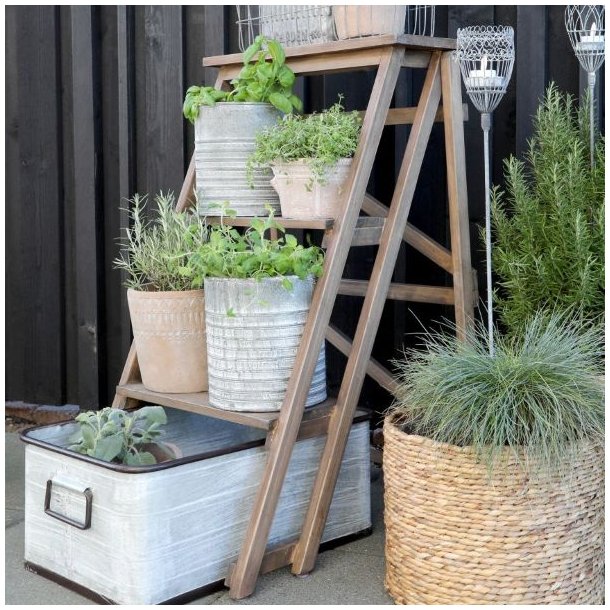 H�j vinkelbillede af den naturfarvede tr�stige p� en terrasse, dekoreret med urtepotter af planter, blomster, krydderurter og metal lanterner.