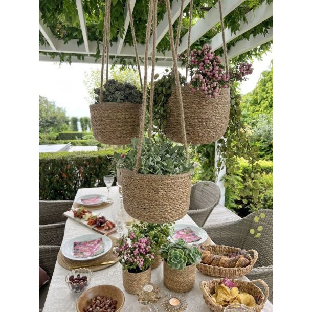 Tre h�ngende urtepotteskjulere i s�gr�s med blomstrende planter oph�ngt ved et d�kket havebord p� en terrasse.