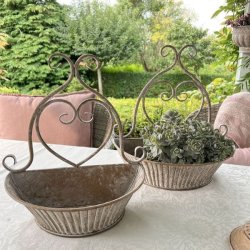 urtepotteskjuler-til-vaeg-sand-patina.jpg S�t med to dekorative v�gurtepotter i jern med gr�nne planter placeret som dekoration p� et hvidt havebord.