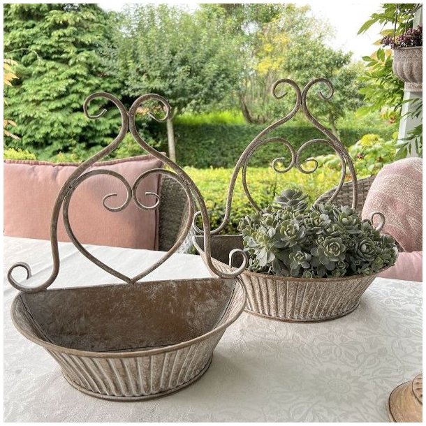 urtepotteskjuler-til-vaeg-sand-patina.jpg S�t med to dekorative v�gurtepotter i jern med gr�nne planter placeret som dekoration p� et hvidt havebord.