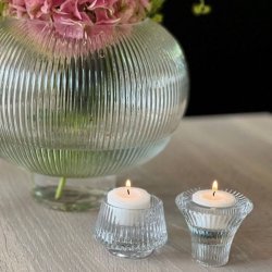 To runde og kegleformede vendbare fyrfadsstager i klart krystalglas opstillet med t�ndte fyrfadslys ved en blomstervase.