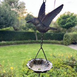 N�rbillede af en fuglefigur og en lille metalsk�l p� vindspillet. Det antikke brune jern ses tydeligt mod den gr�nne havebaggrund.