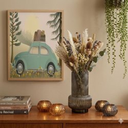 Et kvadratisk 1:1 milj�billede i varm, retro stil, hvor en indrammet Vissevasse plakat i st�rrelsen 30x40 cm h�nger flot og lige p� en beige v�g. Plakaten har motiv af en klassisk, lysegr�n folkevogn bobbel med oppakning p� taget, parkeret i en skovbund med gule blomster under en gylden sol. Under plakaten ses en teaksk�nk pyntet med en r�gfarvet vase med t�rrede blomster og t�ndte glasholdere.