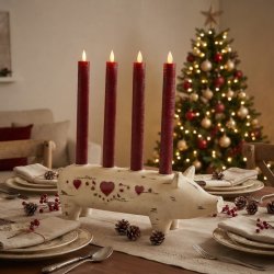 Stemningsfuldt milj�billede af Wilma Gris adventsstage med r�de lys placeret p� et d�kket spisebord med et pyntet juletr� i baggrunden.
