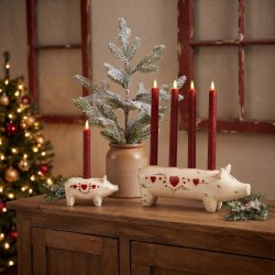 Stemningsfuldt milj�billede af Wilma Gris adventsstage og matchende lysestage med r�de lys, opstillet p� en rustik tr�sk�nk i stuen med et pyntet juletr� og vinduesparti i baggrunden.