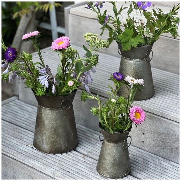Tre zink-urtepotter i forskellige st�rrelser fyldt med farverige blomster og gr�nne st�ngler, opstillet p� en udend�rs tr�trappe.