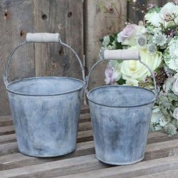 S�t med to rustikke zinkspande i en dekoration p� et tr�bord ved siden af en stor blomsterbuket.