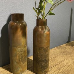 De to kobberfarvede jernvaser st�r sammen med en gren af rosa blomster i den ene vase, placeret p� en gammel tr�b�nk med en m�rkegr� v�g i baggrunden.