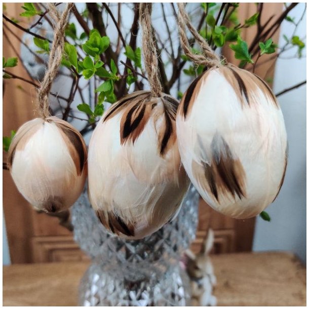 N�rbillede af et creme-farvet p�ske�g med fjer, metaloph�ng og jutesnor, h�ngende p� en for�rsgren.