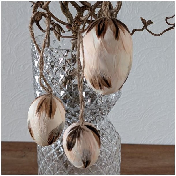 Tre lette creme-farvede p�ske�g med fjer og jutesnor h�ngende dekorativt p� for�rsgrene.